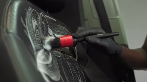 Hand of a Black African American with a Brush Cleans the Leather Seat of a Car