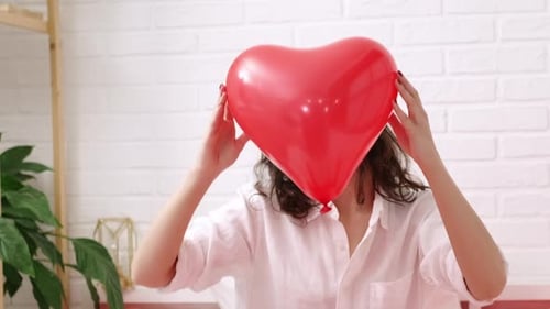 Red Heart Shaped Balloon Close Up in Hands of Brunette Smiling Girl on Valentines Day