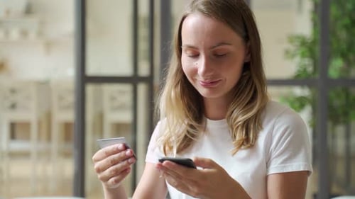 Woman Holding Credit Card and Smartphone. Young Woman Sitting on Sofa Spend Money at Home, Make