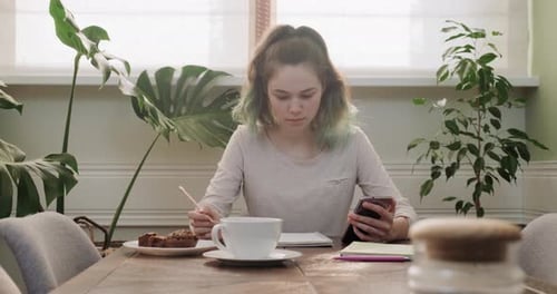 Young Woman Writing at a Table with Phone