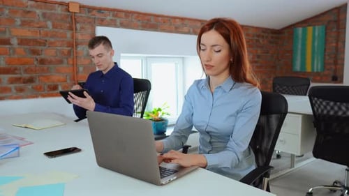 Beautiful Female Office Worker Works on Her Laptop While Her Male Colleague Uses Calculator