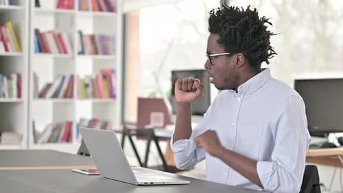 Man Coughing While Working at Computer Indoors