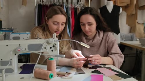Two fashion designers looking at samples of fabric near sewing machine in a sewing workshop