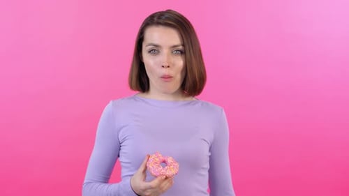 Woman Eating a Pink Frosted Donut in Studio