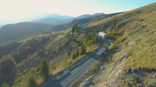 Aerial View Of Big Cargo Trucks Passing Each Other on Winding Mountain Road in Sunny Autumn Day in