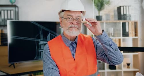 Trabajador de la construcción con casco y chaleco que se quita las gafas mientras mira a la cámara