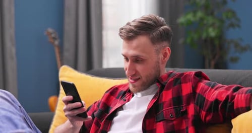 Man Relaxing on Couch Using Smartphone