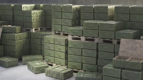 Huge stack of ammo boxes with RPG missiles and rifle ammunition in warehouse.
