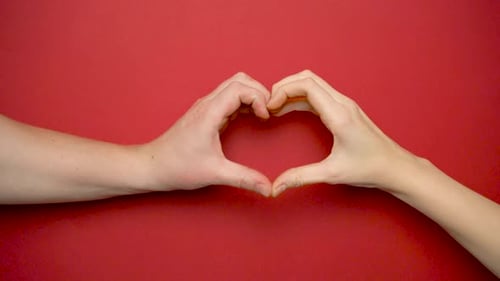 Close-up of a female and male hand making a heart on a red background.