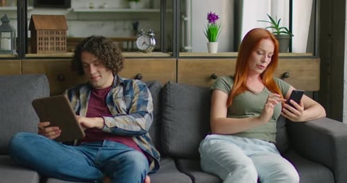 Young Couple Using Devices Sitting on Sofa