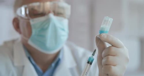 Close Up Shot of Unrecognizable Nurse or Doctor in Gloves Filling Syringe From Ampule with Covid-19