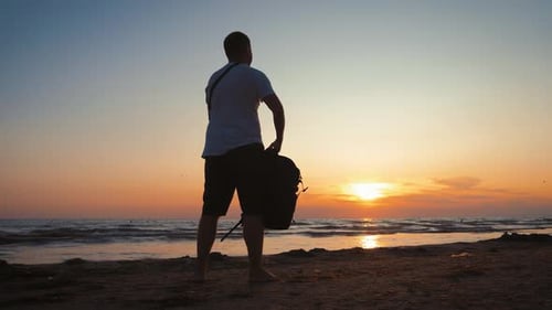 Silhouette des Reisenden mit Rucksack genießt den Sonnenuntergang am tropischen Meeresstrand. Reisen entlang der Küste