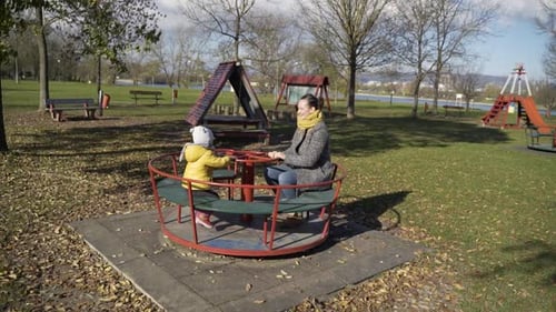 Mother and son playing at merry-go-round in public playground, Zagreb, Croatia.