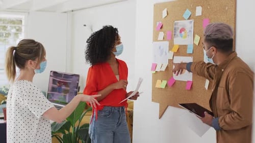 Office colleagues wearing face mask discussing over memo notes at office