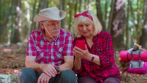 Attractive Senior Old Man Woman Backpacker Planning Trip Route in Forest on Mobile Phone in Wood