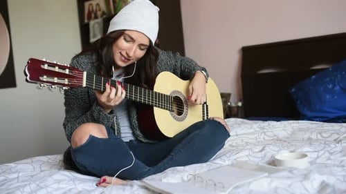 Woman Plays Guitar and Sings in Bedroom