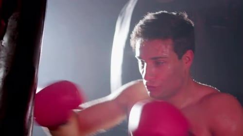 Shirtless Man Punching Heavy Bag With Boxing Gloves