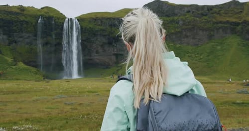 Nahaufnahme einer Frau mit Rucksack, die den berühmten Seljalandsfoss-Wasserfall Island genießt