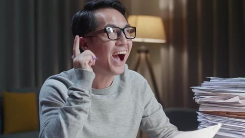 Close Up Of Asian Man Thinking And Looking At Paper Then Raising Index Finger While Working