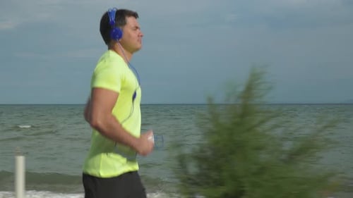 Man Jogging on a Beach with Headphones