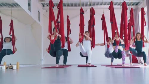 Ladies Practice Modern Fly Yoga and Stand in Warrior Pose
