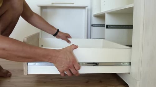 Close up of male carpenter hands assembling furniture cupboard and installing wooden new drawer.