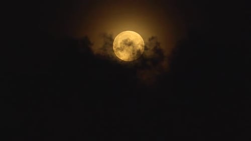 Full Moon Rising Behind Dark Clouds at Night