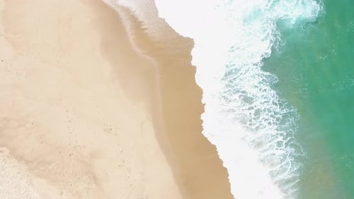 Aerial view waves break on white sand beach. Shot on Phantom 4