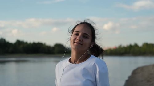 A Woman in Headphones Runs at a Beautiful Sunset on the Beach, Sun Glare From the Water. Sport and