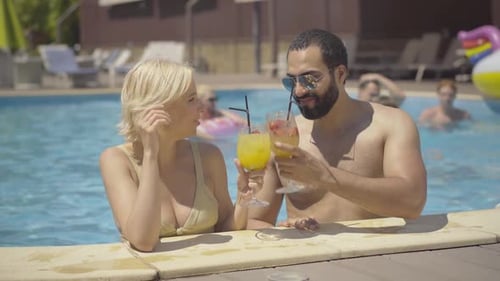 Cheerful Interracial Couple Clinking Glasses and Drinking Cocktails in Pool. Portrait of Happy