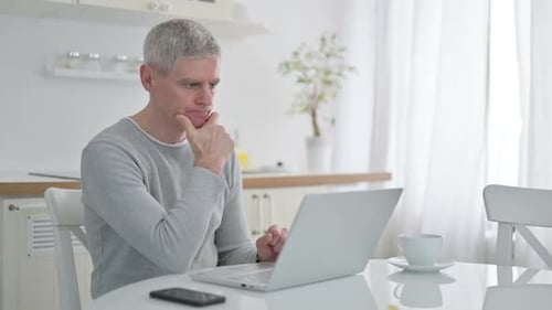 Man Thinking with Laptop at Table at Home