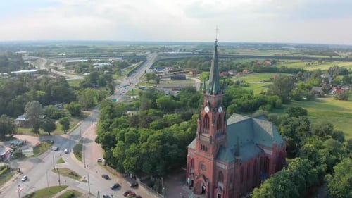 Church in Small City Among Pastures. Drone Footage. Red Church Is Roman Catholic Church.
