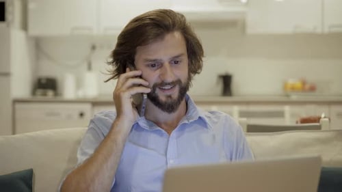 Man on Couch Talking on Phone with Laptop