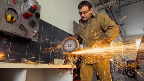 Un trabajador que usa una amoladora corta metal en un taller