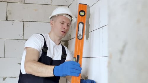 Beautiful Young Architect or Builder in a White Hard Hat Checks the Level of the Wall with the Level