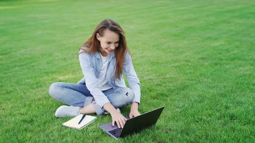 Happy Woman Working on Laptop Computer on Green Lawn in Summer Park