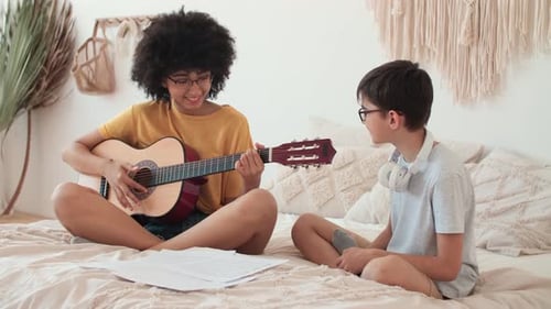 Teenage Girl Plays Guitar for Boy in Bedroom