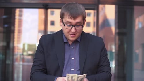 A Businessman Counts Money Standing Near the Business Center