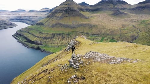 Flying Around a Hiker at the Top of a Mountain Above Funningur on Faroe Islands