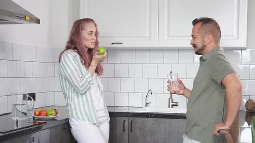 Couple Talking in Modern Kitchen With Apple and Glass