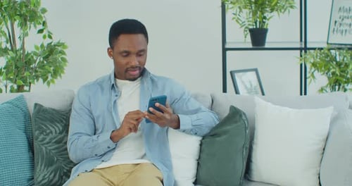 AfricanAmerican Guy Using Smartphone for Messaging Scrolling News Reading Feeds in Social Media