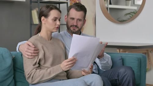 Couple Reading Documents Together on Sofa at Home