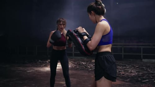 4K Asian woman boxer practicing boxing with female coach in abandoned building.