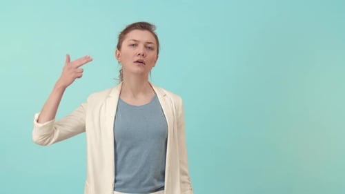 Deprimierte Frau gestikuliert Pistole mit Hand und schießt Kopf auf blauem Hintergrund im Studio