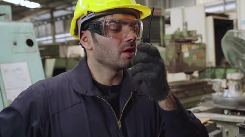 Fabrikarbeiter spricht mit tragbarem Radio, während er Maschinenteile inspiziert