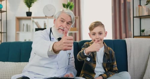Un pédiatre barbu regarde la caméra avec un adolescent souriant et faisant des gestes du pouce vers le haut