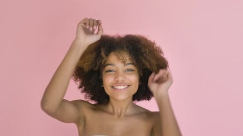 Cheerful Woman Dancing with Curly Hair on Pink