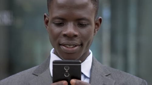 Smiling Man Looking at Phone in Urban Setting