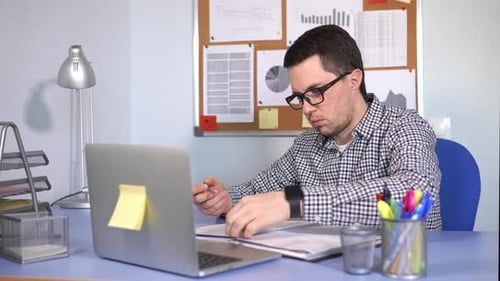 Man Reviews Documents at Desk with Laptop
