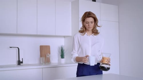 Woman Pours a Cup of Coffee in Kitchen
